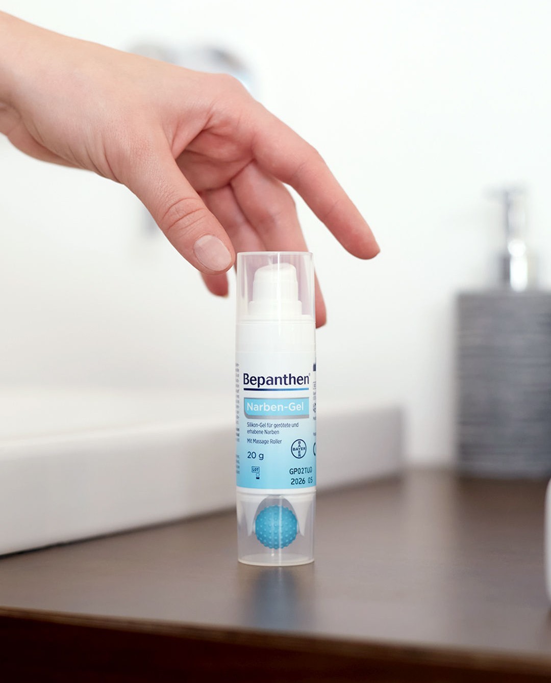 Bepanthen Narben-Gel on a bathroom counter, a hand entering the frame, domestic everyday