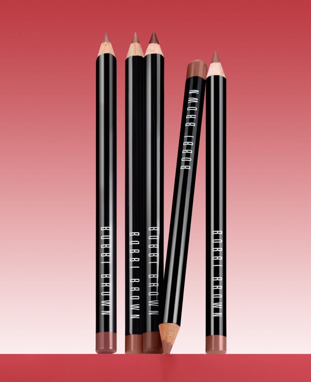 Bobbi Brown lip pencils standing on a red gradient surface